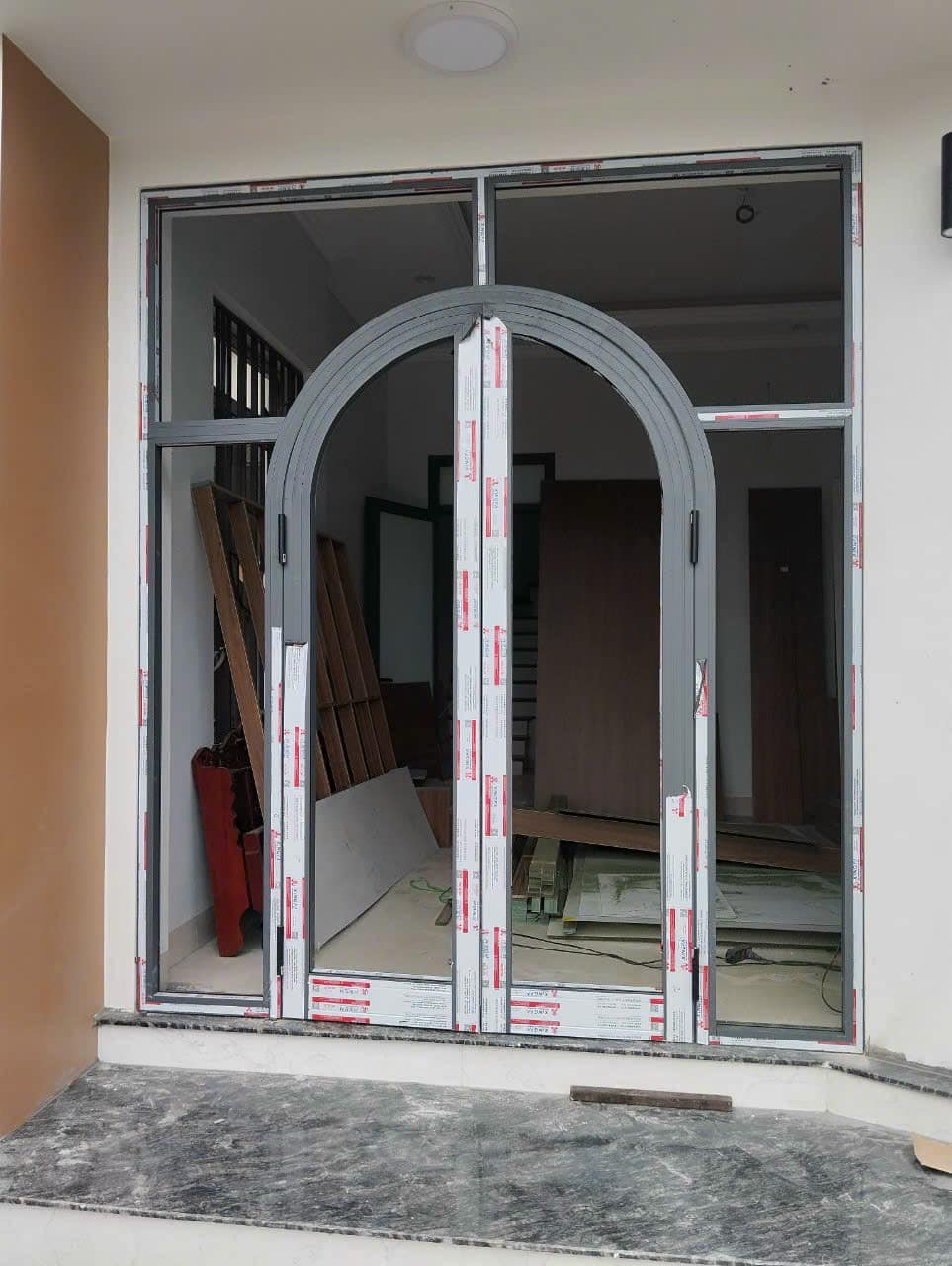 Cửa nhôm kính khung vòm màu xám đang lắp đặt cho mặt tiền nhà đang thi công